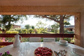 A table set for dining with a pitcher, glasses, and a bowl of fruit, overlooking a scenic landscape with trees and buildings. - Villa Giolù (Portoferraio)
