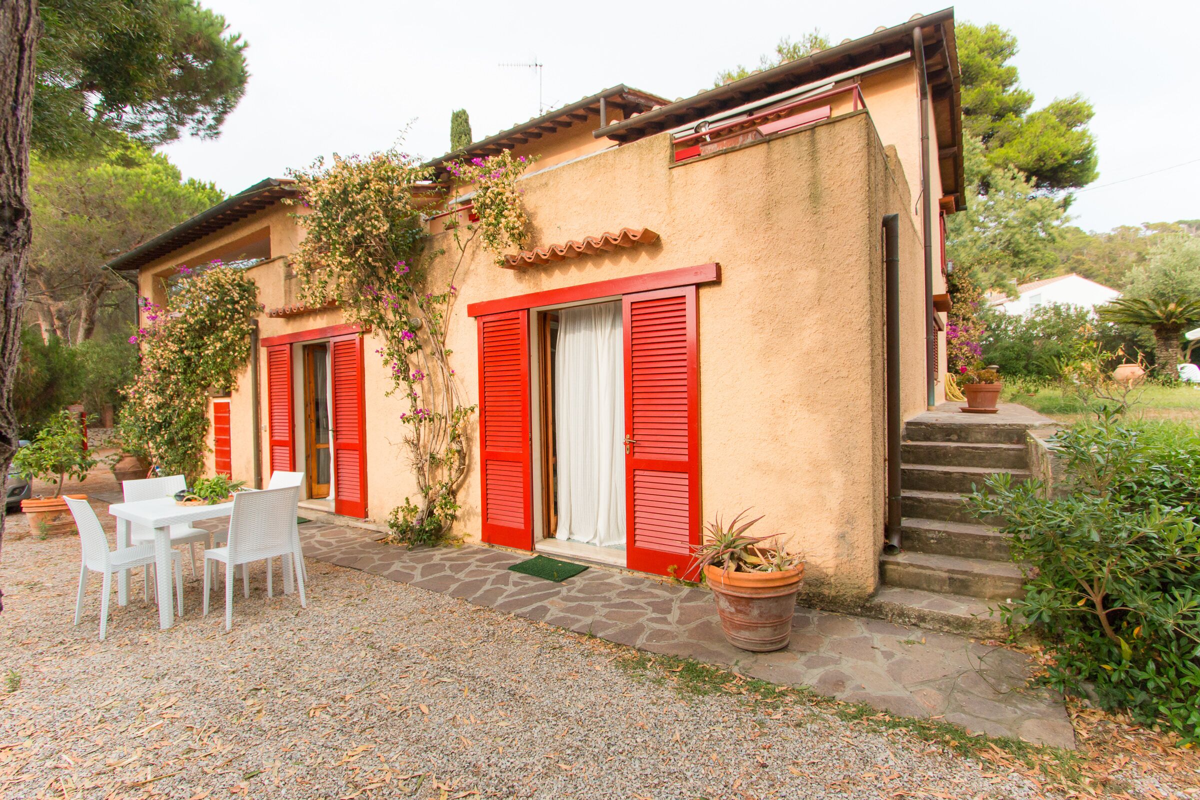 A rustic building with red shutters, a stone pathway, and a table with chairs outside.