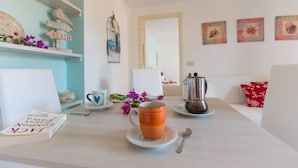 A room with a white sofa, a coffee table with a book, a mug, and a coffee maker. There are decorative items on shelves and a mirror on the wall. - Villa Giolù (Portoferraio)
