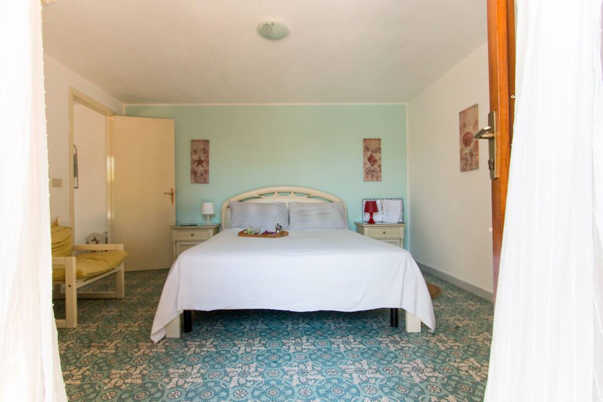 Quarto com cama, mesas de cabeceira e uma cadeira.