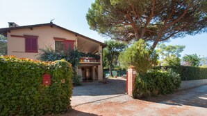 A house with a covered porch, a gravel driveway, and a large tree in front. - Villa Giolù (Portoferraio)