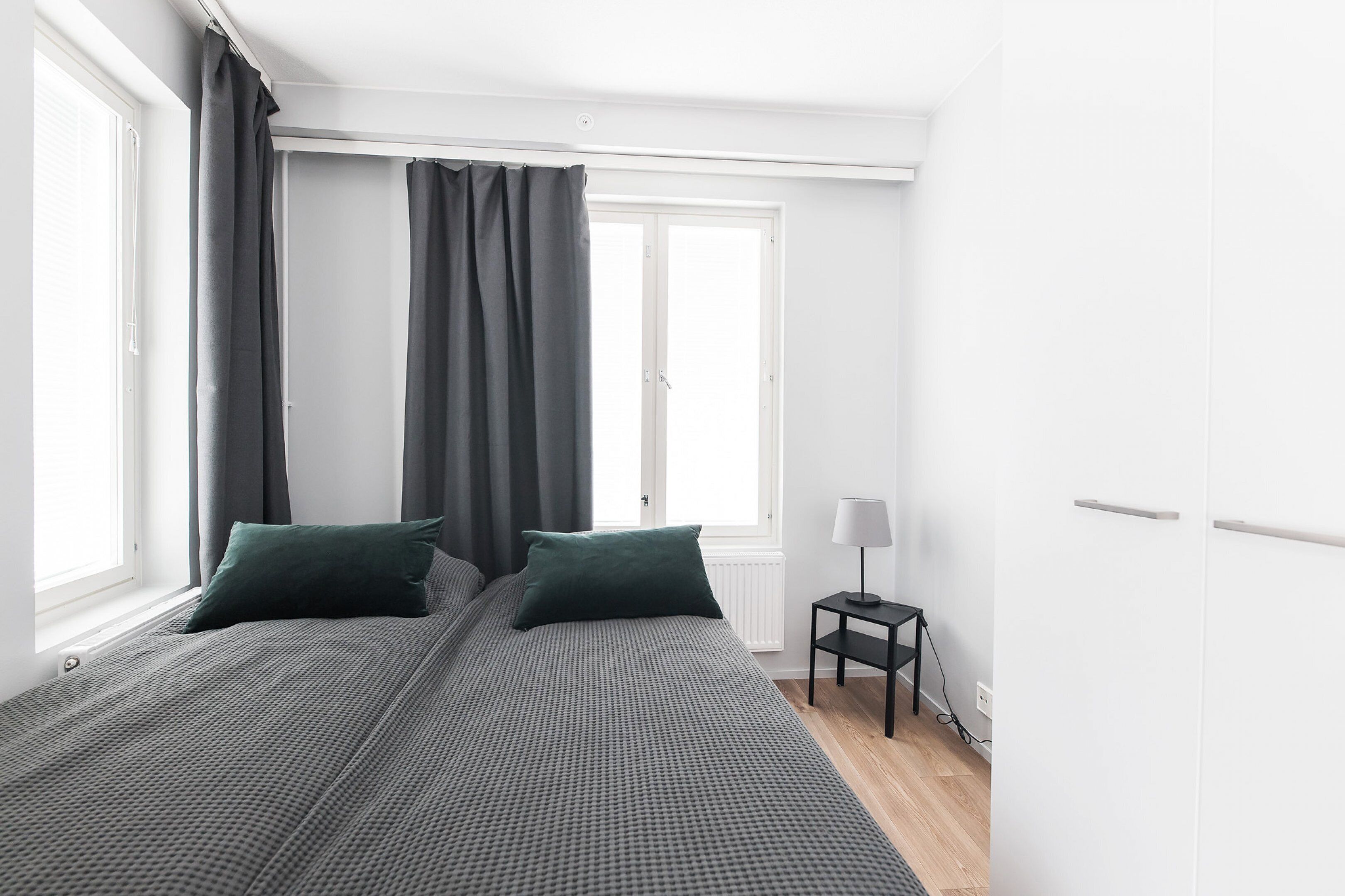 A bedroom with a large bed, two pillows, a nightstand with a lamp, and a window with curtains.