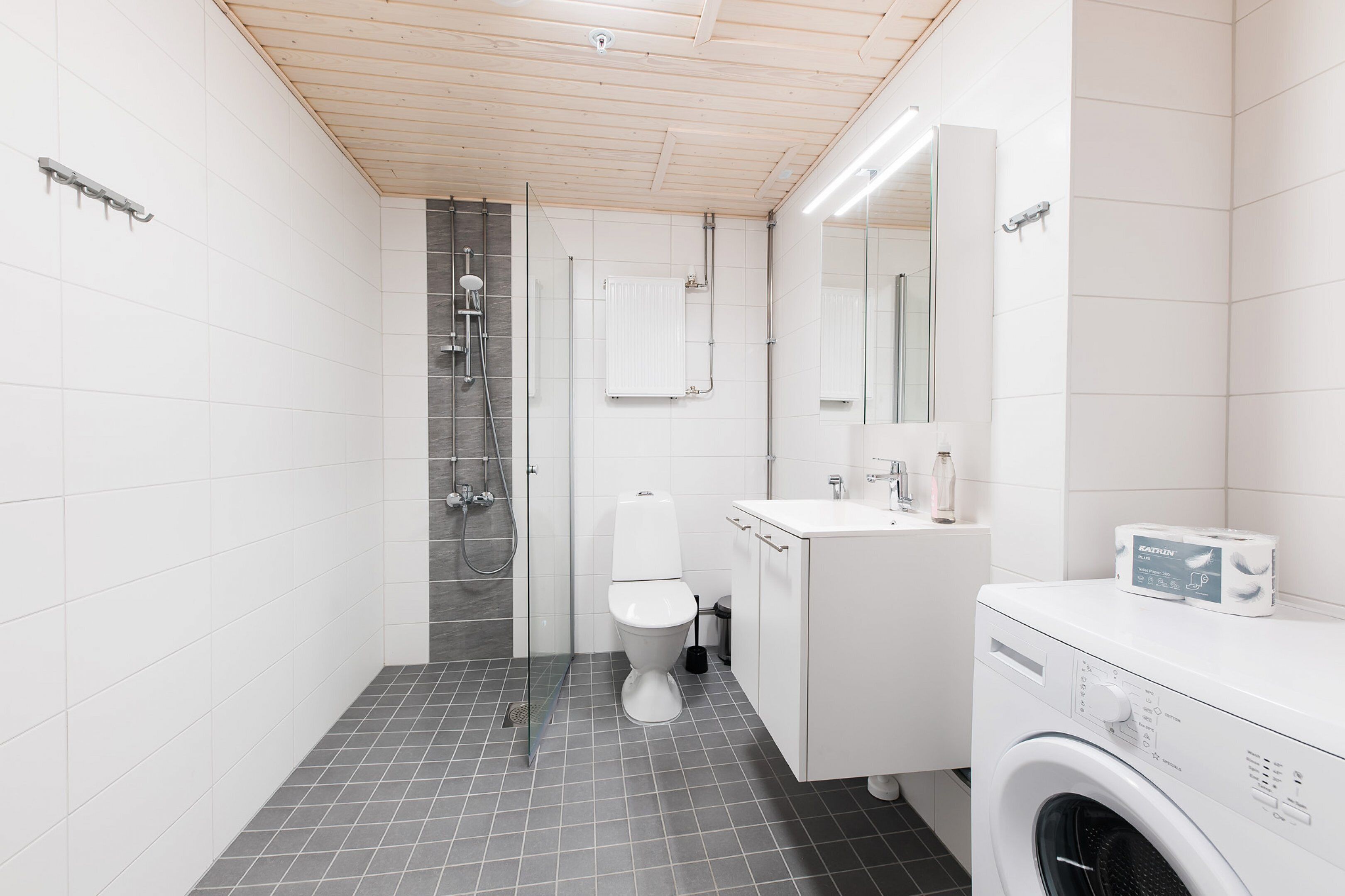 A modern bathroom with a shower, toilet, and a washing machine.