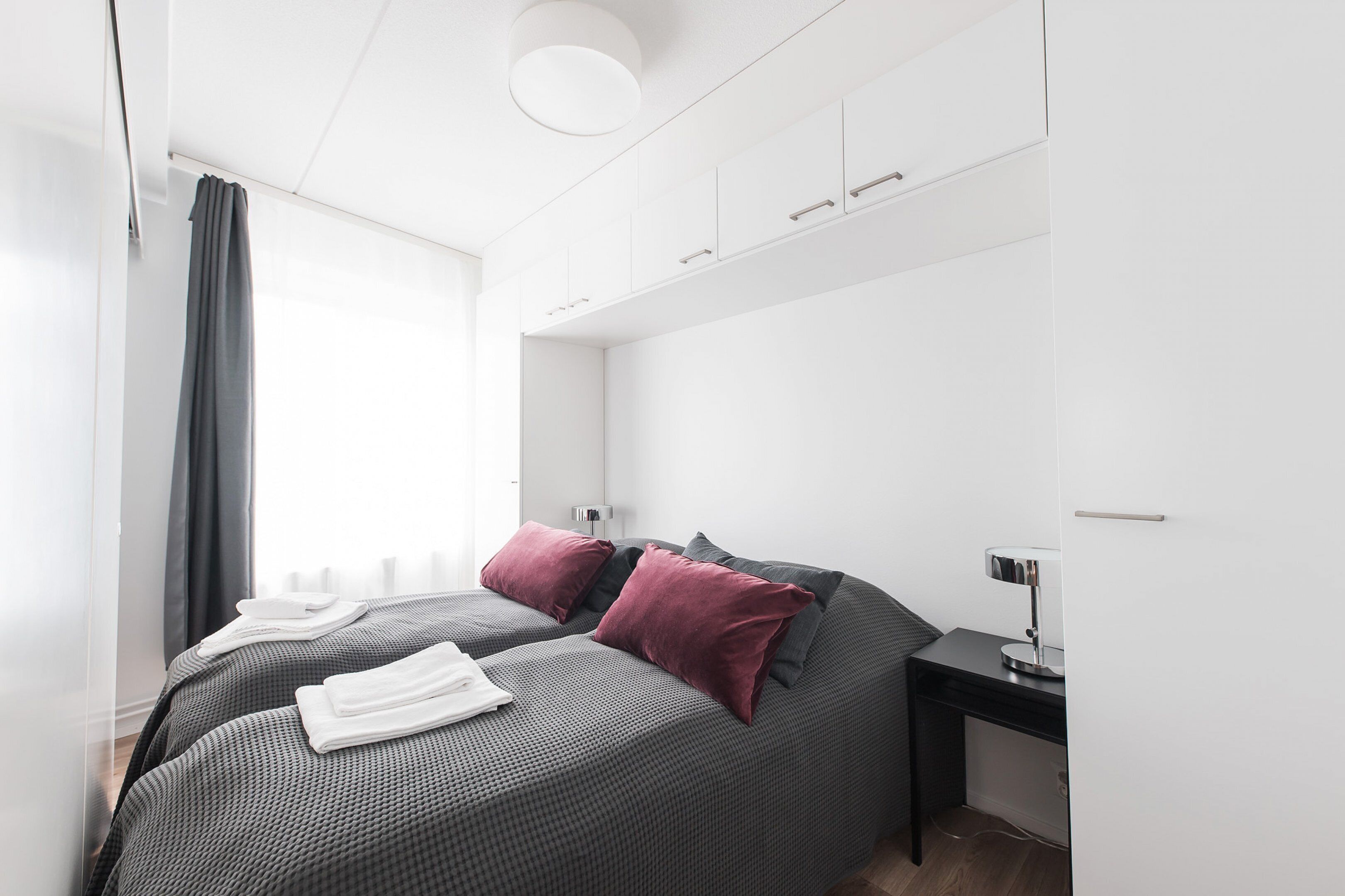 Une chambre moderne avec deux lits, une literie aux couleurs sombres et une table de chevet avec une lampe.