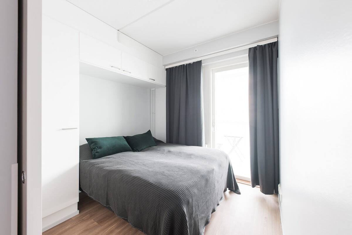 Une chambre à coucher moderne avec un lit, des rideaux foncés et une armoire blanche.