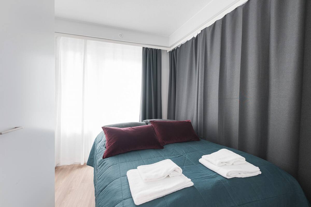 Un lit bien fait, recouvert d’une couvre-lit turquoise, avec deux oreillers rouge foncé et des serviettes blanches pliées.