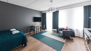 A modern hotel room with a bed, a desk, a chair, a sofa, and a TV. - Forenom Serviced Apartments Neilikkatie (Vantaa)