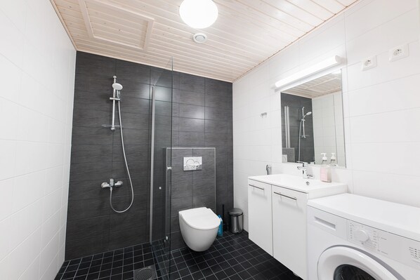 A modern bathroom with a shower, toilet, sink, and washing machine.