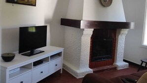 Una sala de estar con chimenea, un televisor sobre un mueble blanco y un cuadro en la pared.