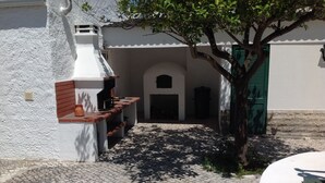 Un patio con zona de barbacoa, un sendero de adoquines y un edificio blanco con puerta verde.