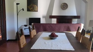 Comedor con mesa redonda, sillas tejidas, un recipiente en el centro y una lámpara colgante.