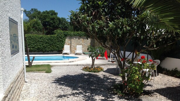 Un área de piscina con un patio de piedra, dos sillas blancas y una escultura roja.