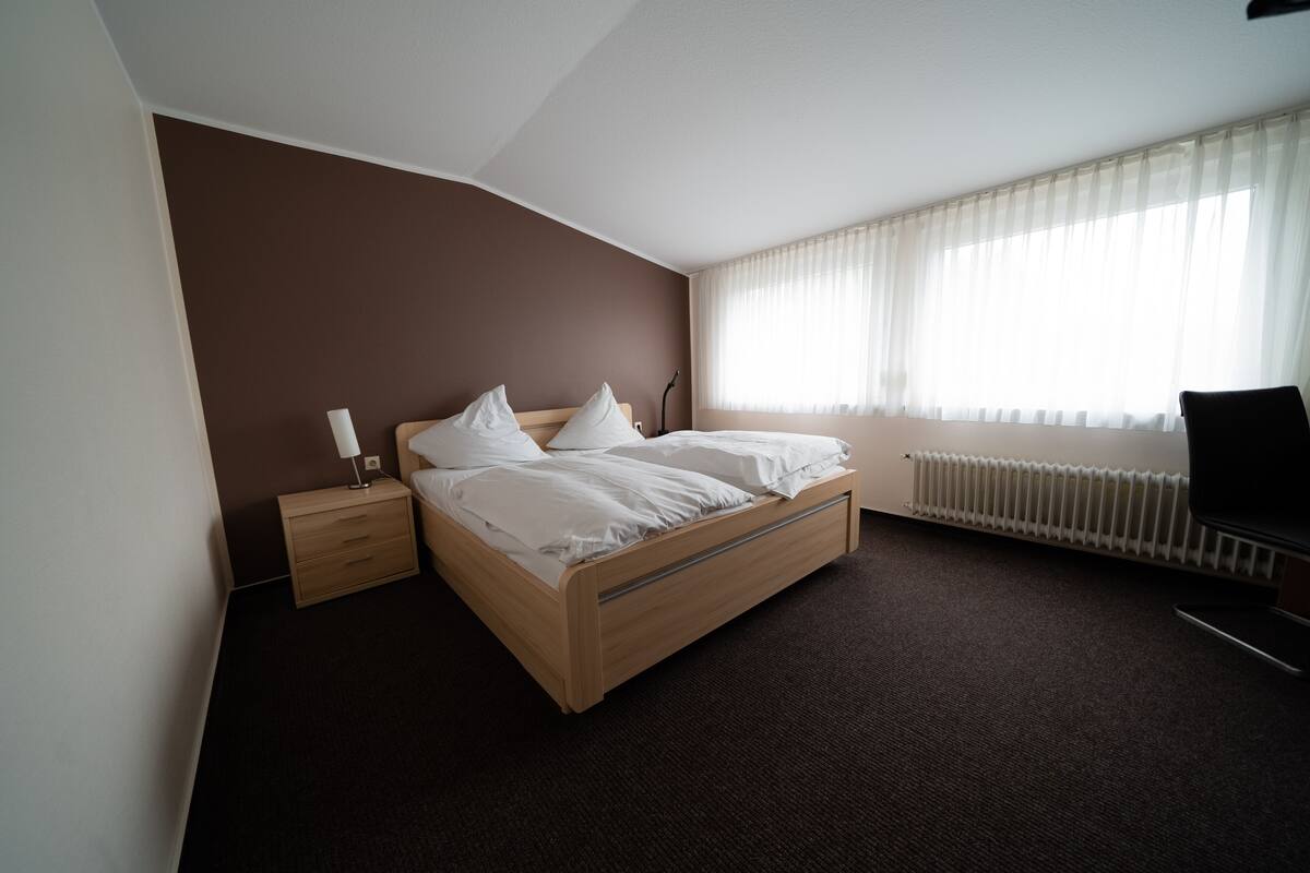 A bedroom with a bed, a nightstand, a chair, and a radiator.