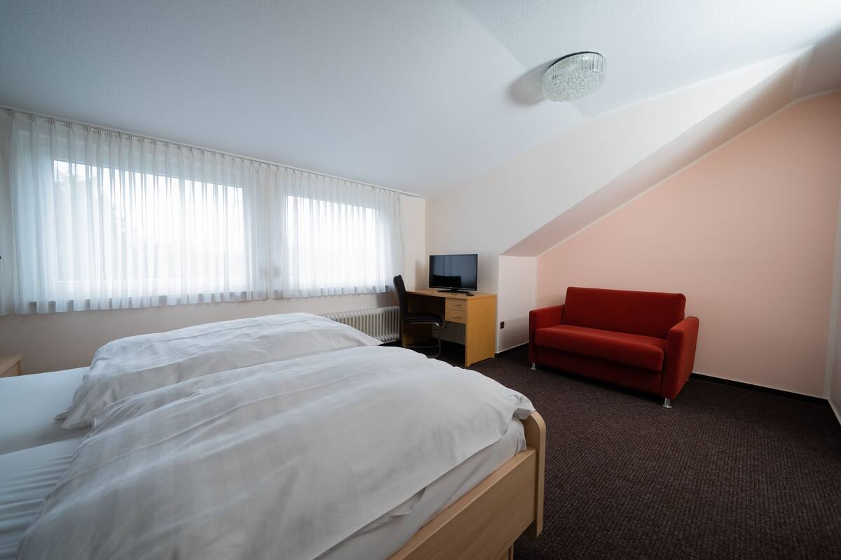 A hotel room with a large bed, a desk with a computer, a red chair, and a television.