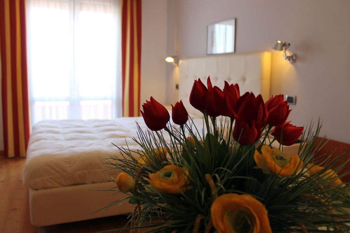 Una habitación de hotel con una cama, una lámpara de pared y una ventana con cortinas.