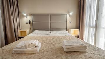 Habitación de hotel con una cama grande, dos mesitas de noche, cabecero y una ventana con cortinas.