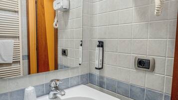 Un baño con lavamanos blanco, espejo, toallero y secador de pelo montado en la pared.