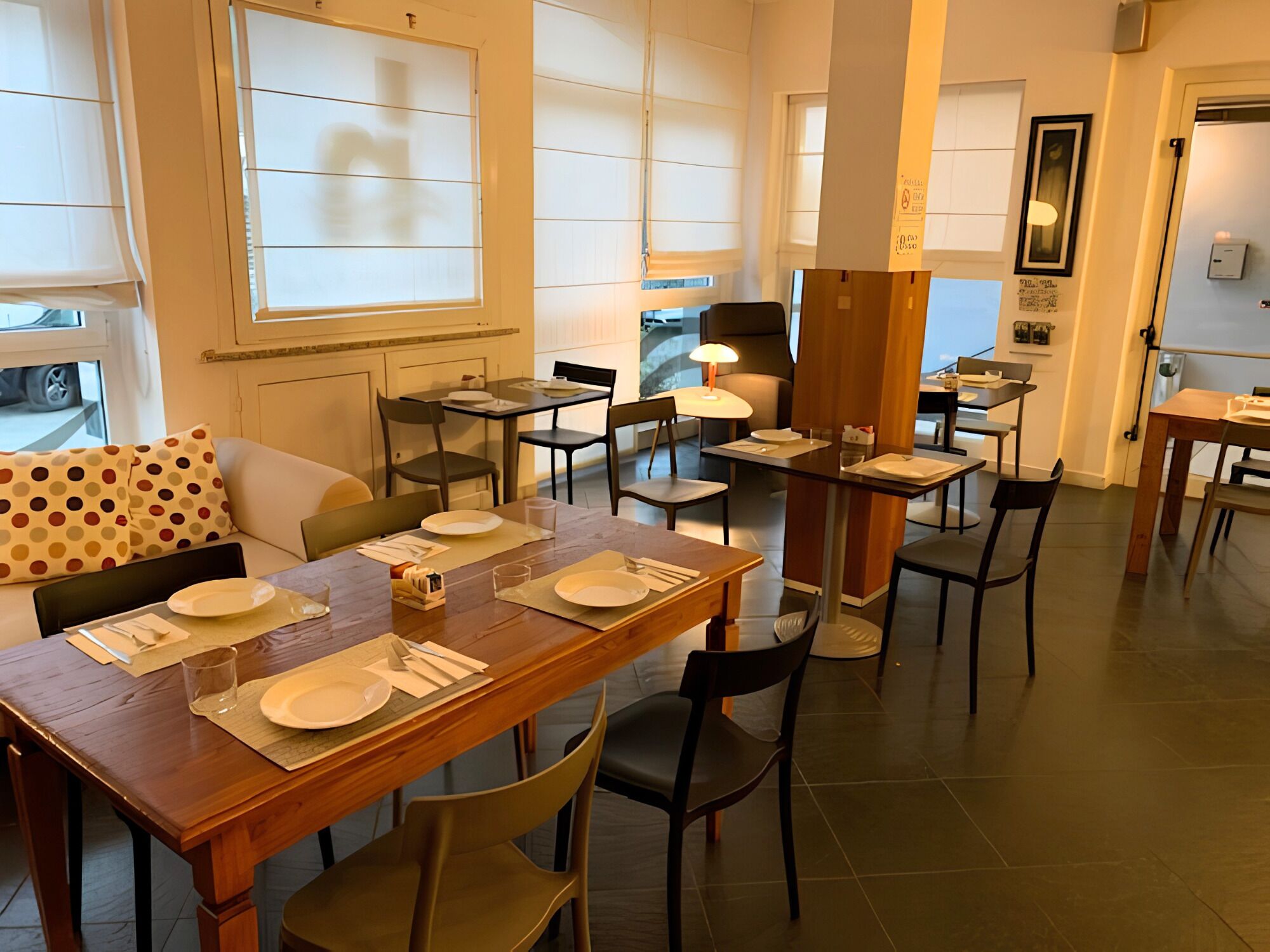 Un comedor con mesas dispuestas para cuatro, sillas y un sofá con un cojín de lunares.