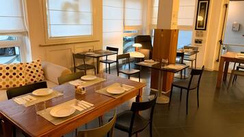 Un comedor con mesas dispuestas para cuatro, sillas y un sofá con un cojín de lunares.