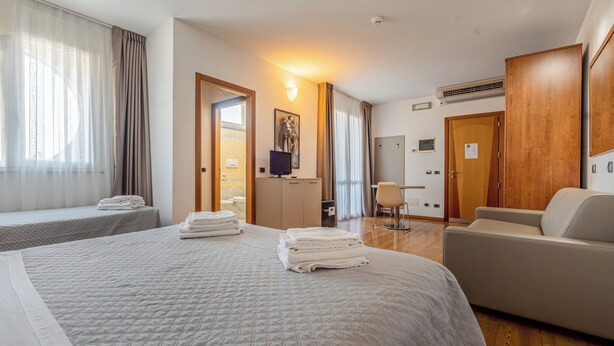 A hotel room with two beds, a sofa, a desk, and a television. - Rubicone Hotel (Savignano sul Rubicone)
