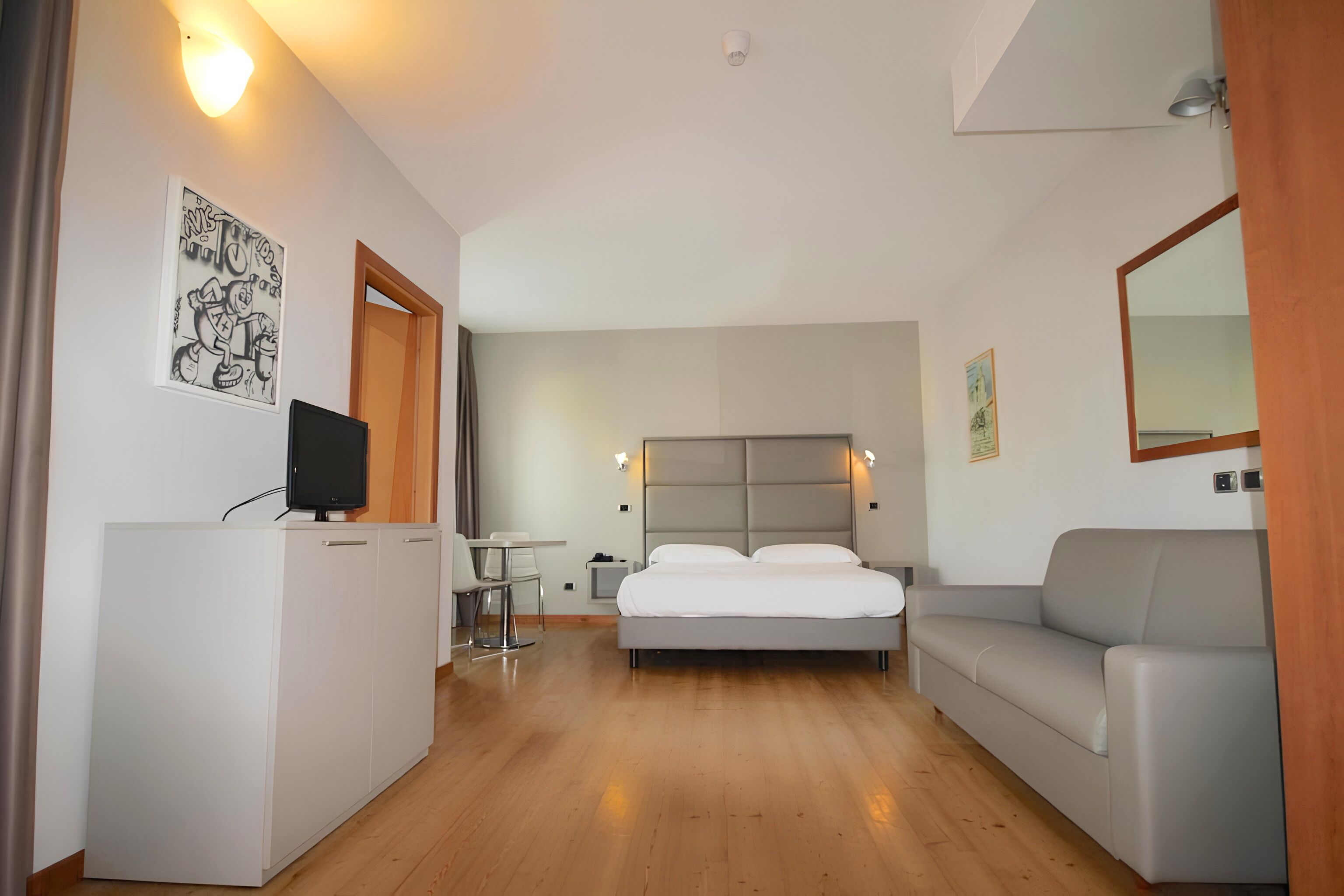 Une chambre d’hôtel avec un lit, un bureau, une télévision, un canapé et un miroir.
