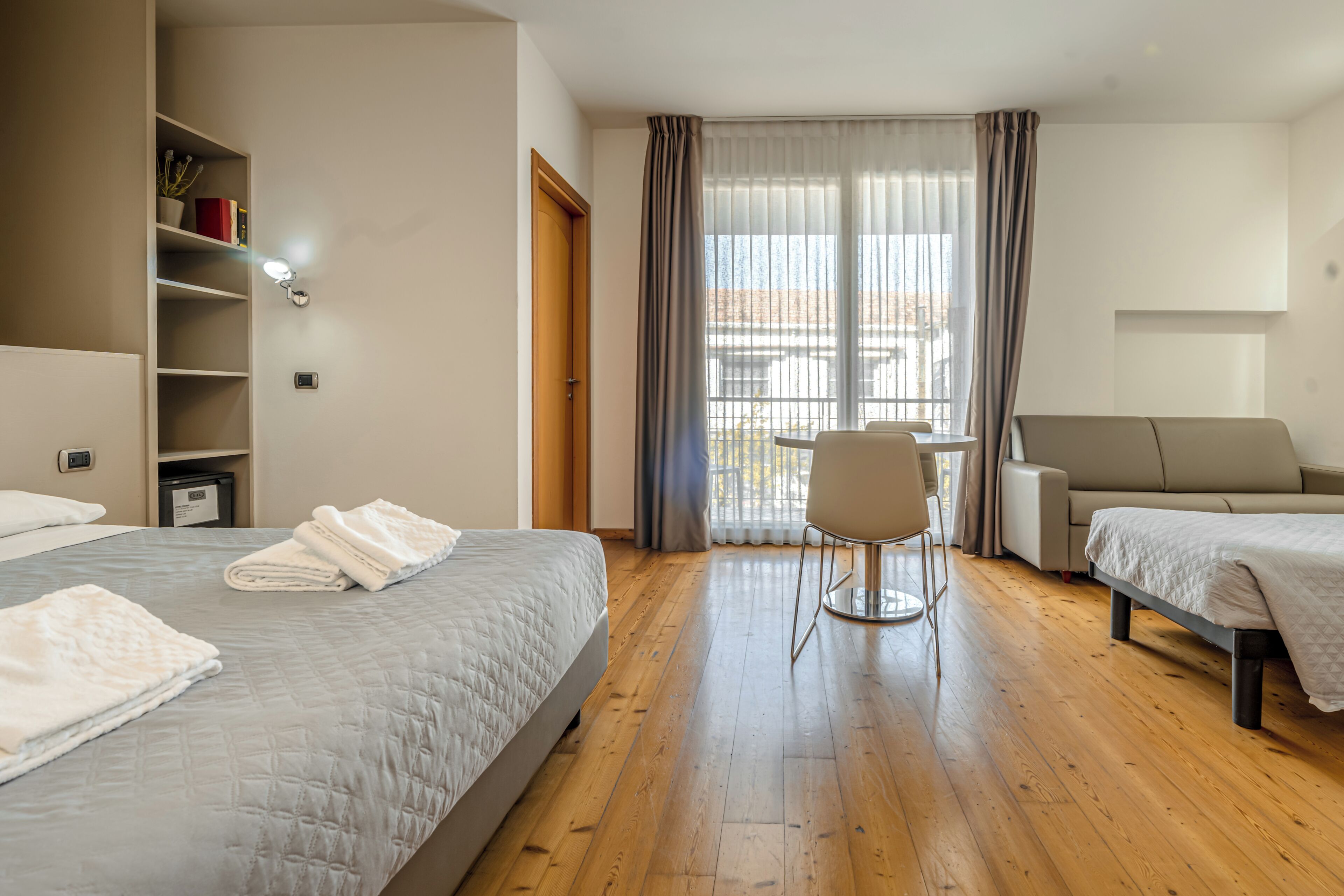 Quarto de hotel com duas camas, uma escrivaninha, uma cadeira e um sofá.