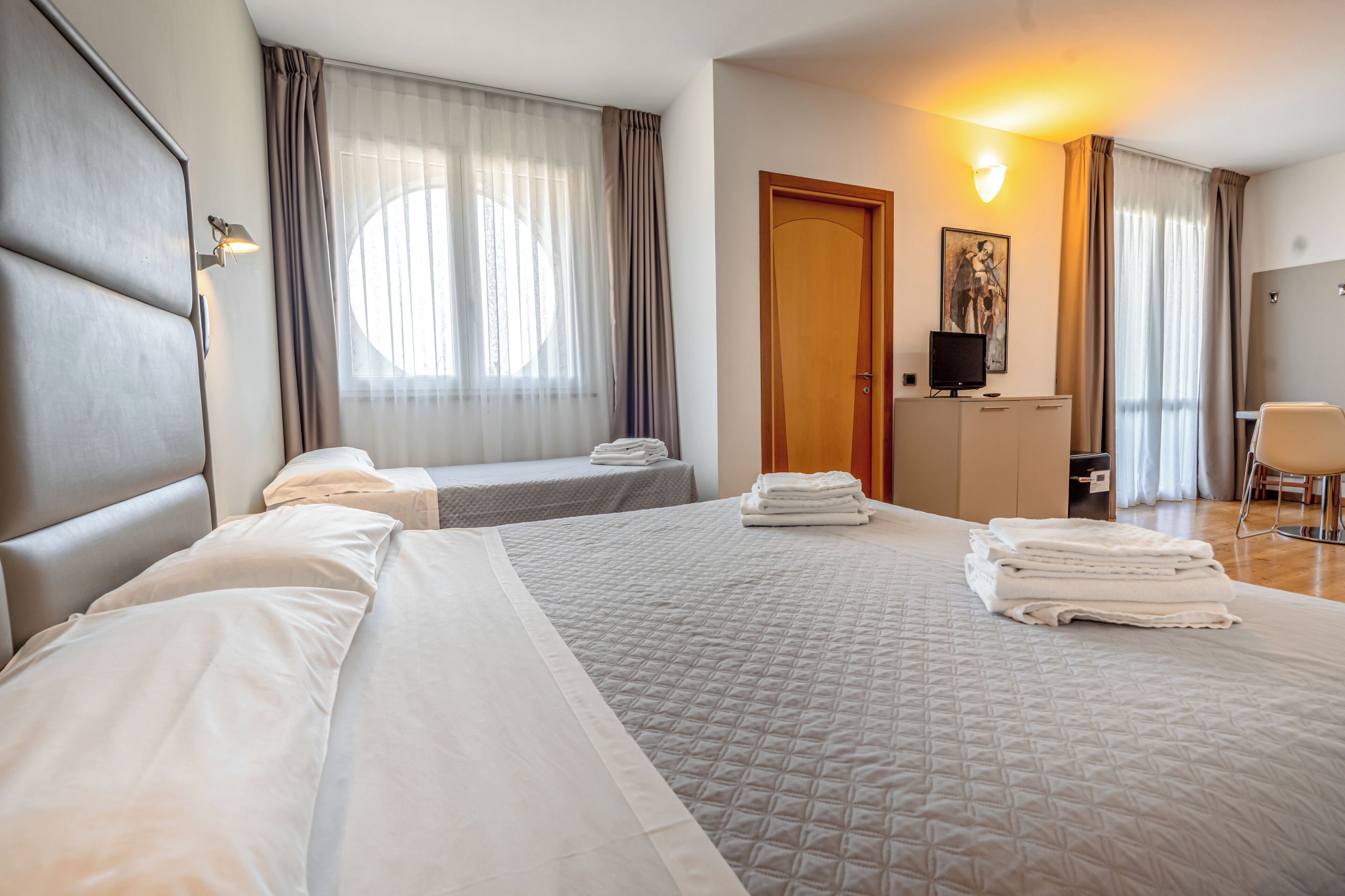 A hotel room with two beds, a desk, a chair, and a television.