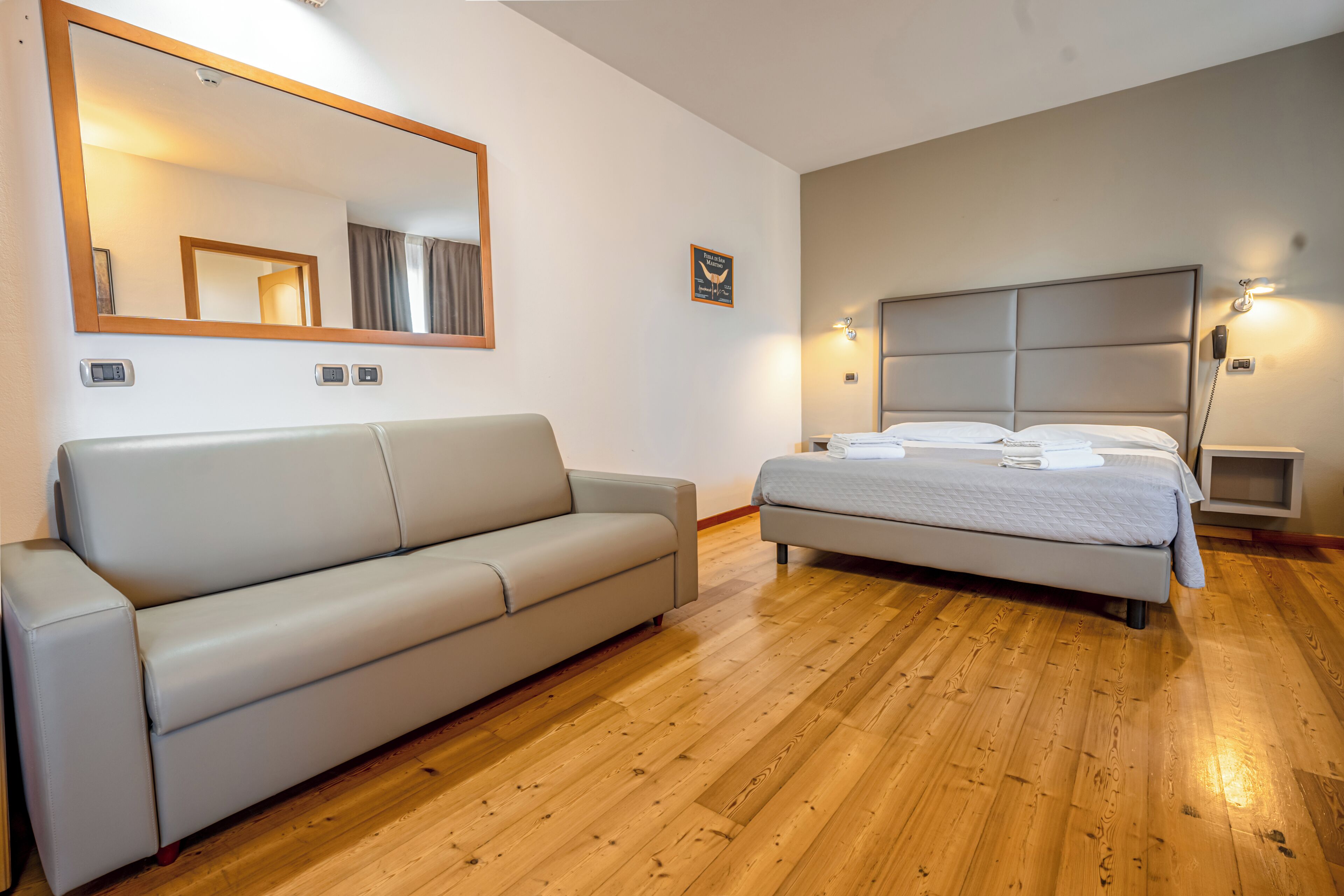 A bedroom with a bed, a sofa, a large mirror, and a nightstand.