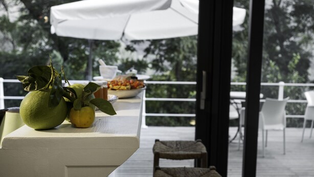Una mesa con un cuenco de fruta y un paraguas blanco en una terraza al aire libre.