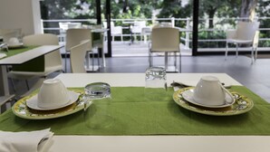 Una mesa de comedor con dos tazas blancas sobre posavasos verdes, un vaso y una servilleta.