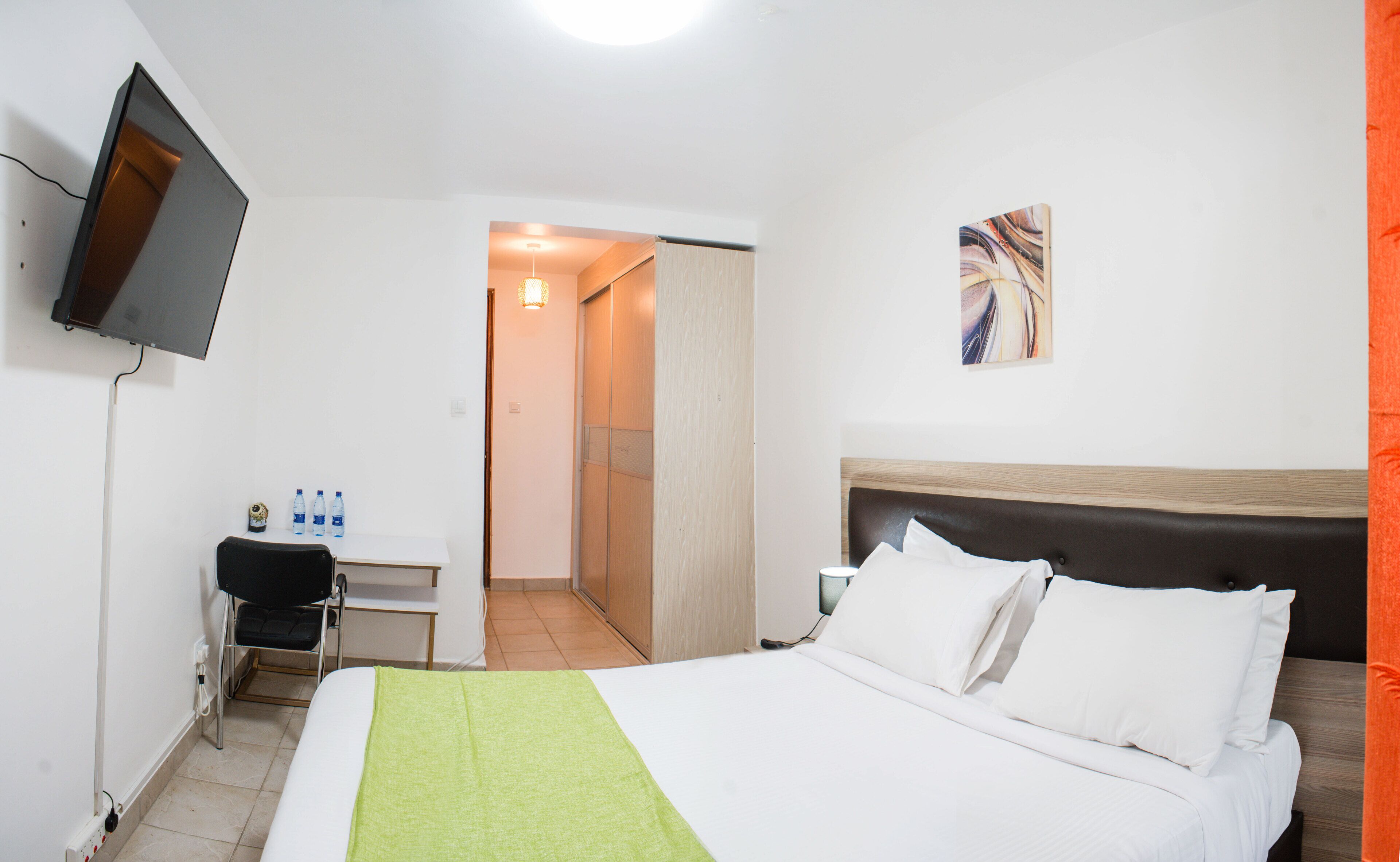 Ein Hotelzimmer mit einem Bett, einem Schreibtisch, einem Sessel, einem Fernseher und einem Bild an der Wand.