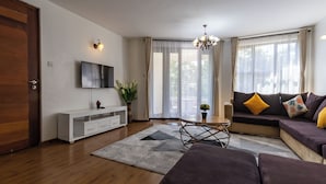 A modern living room with a sofa, a TV mounted on the wall, a wooden floor, and a chandelier. - Erica Residences (Nairobi)