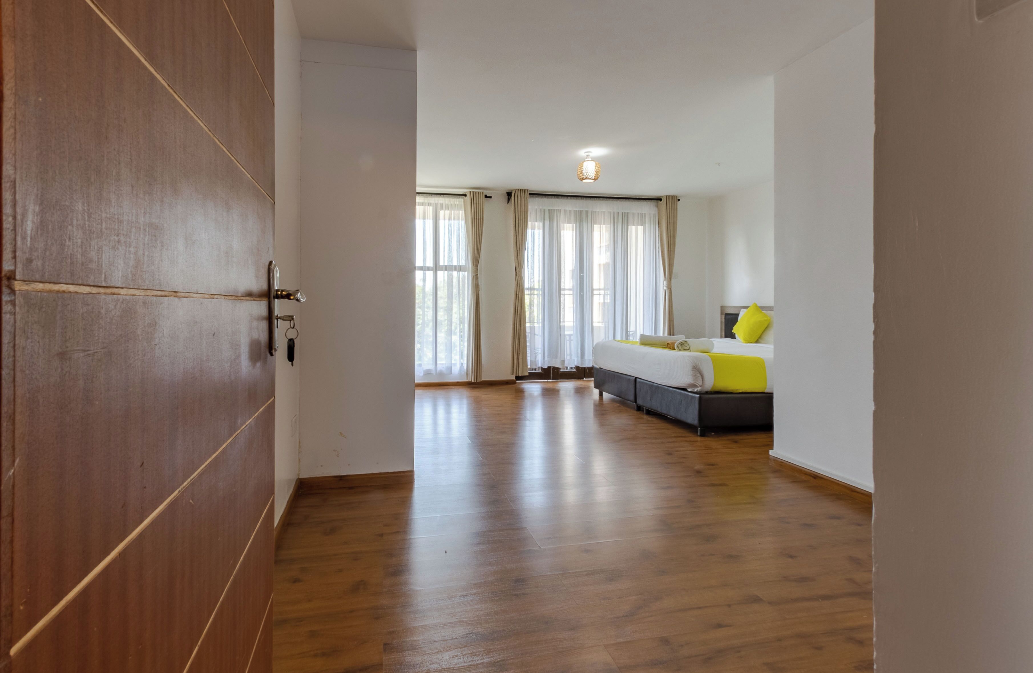 A room with a wooden floor, a bed with a yellow and gray headboard, and a window with curtains.