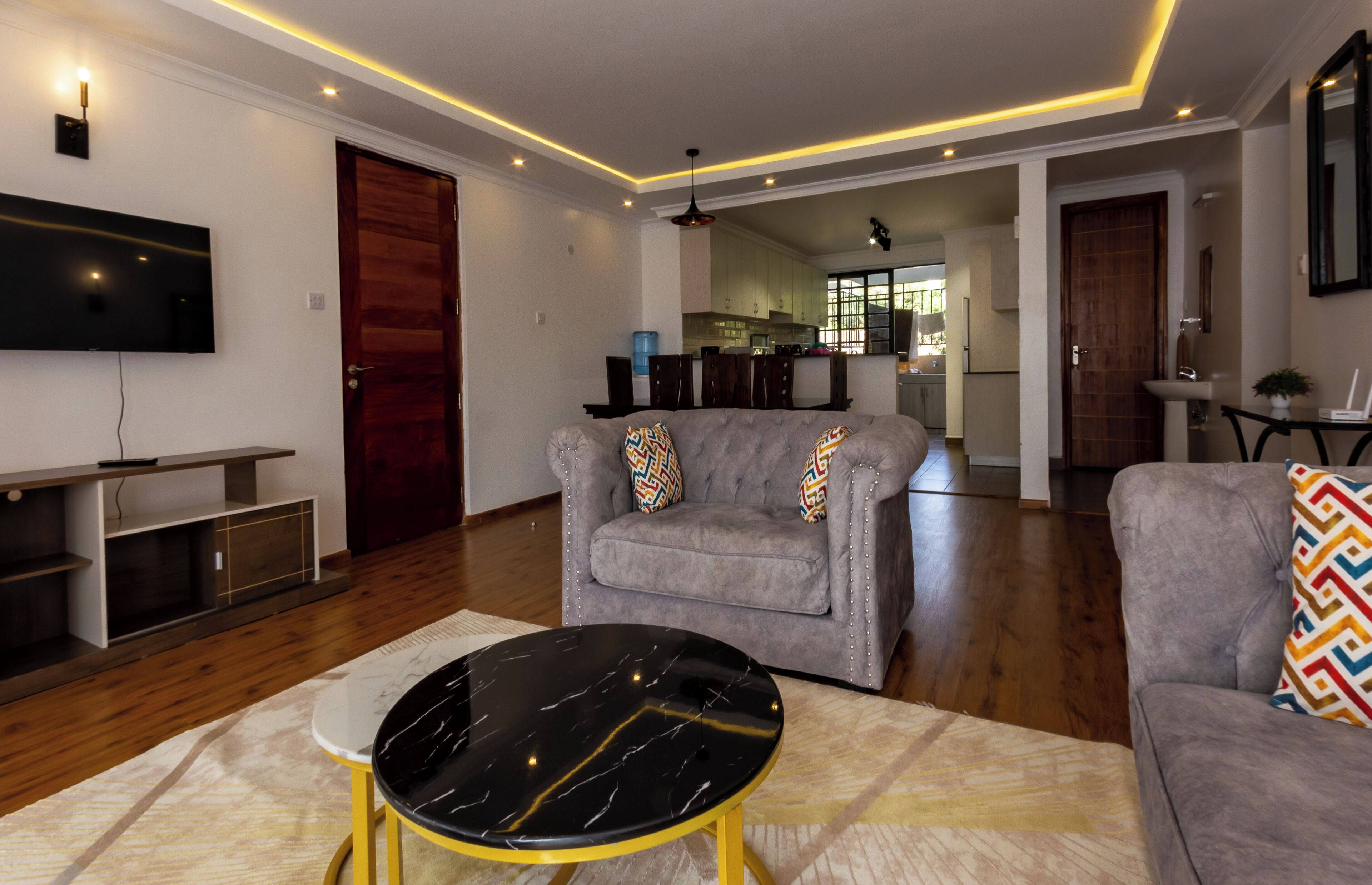 A modern living room with a grey sofa, a black marble coffee table, and a TV mounted on the wall.