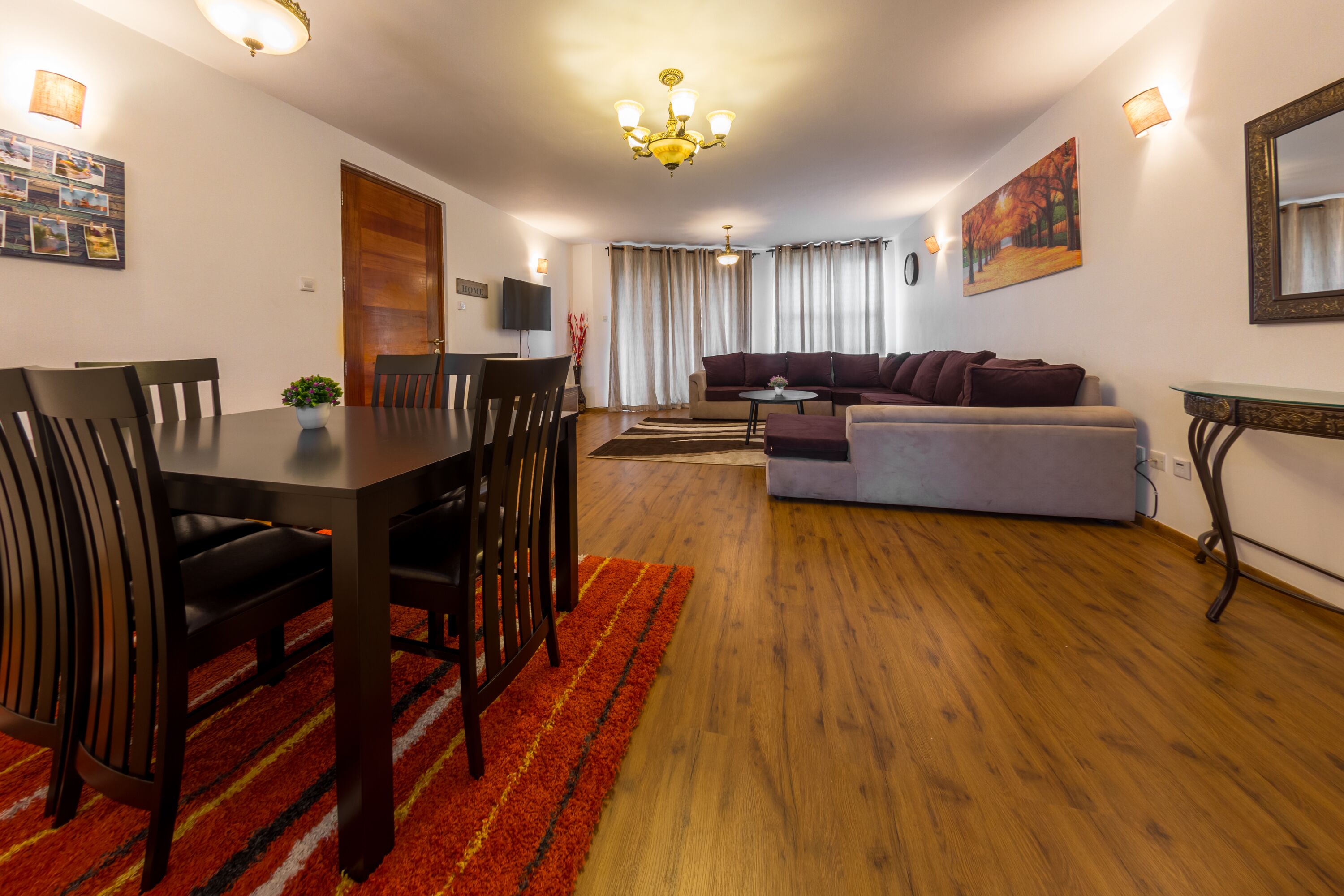 Ein modernes Wohnzimmer mit Essbereich, Holzboden und einer Chandelüster.