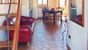 Un vaste espace de vie doté d’un plafond en bois surélevé, d’un canapé en cuir rouge, d’une table à manger avec des chaises et d’un coin cuisine visible à travers une porte ouverte.