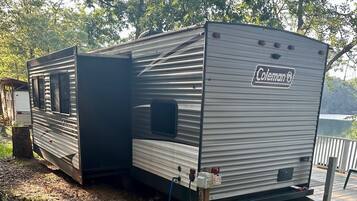 Een Coleman RV geparkeerd buiten, met een overdekt terras en uitzicht op een meer.