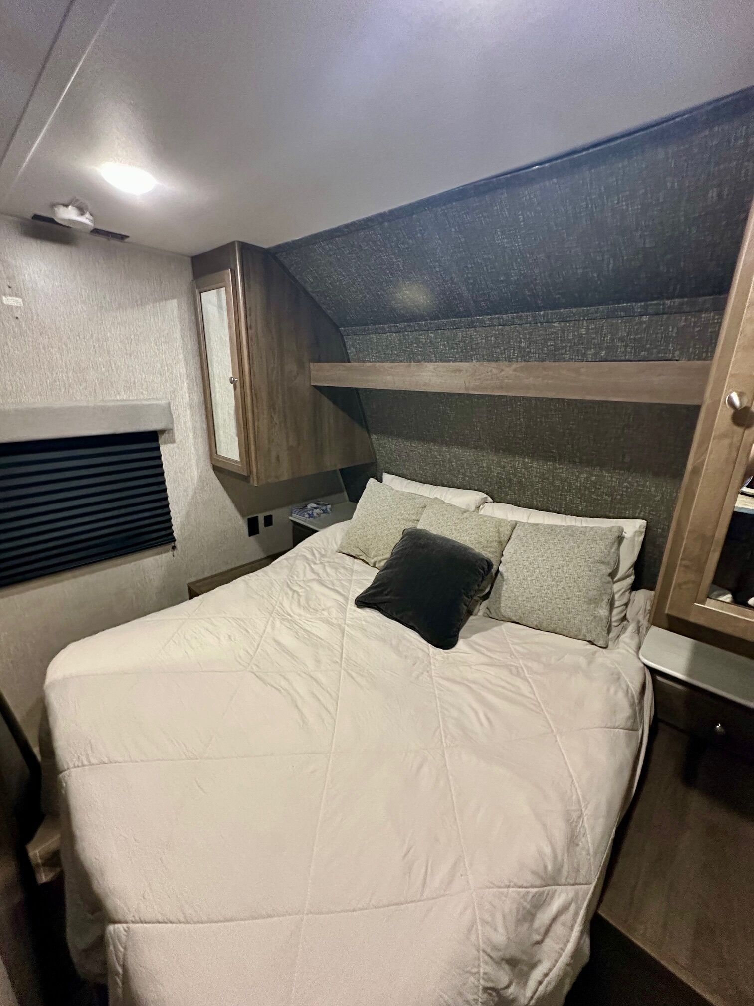 Een stapelbed met een wit matras en kussens, een klein raam met zonwering, en een houten hoofdbord.