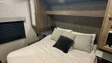 Een stapelbed met een wit matras en kussens, een klein raam met zonwering, en een houten hoofdbord.
