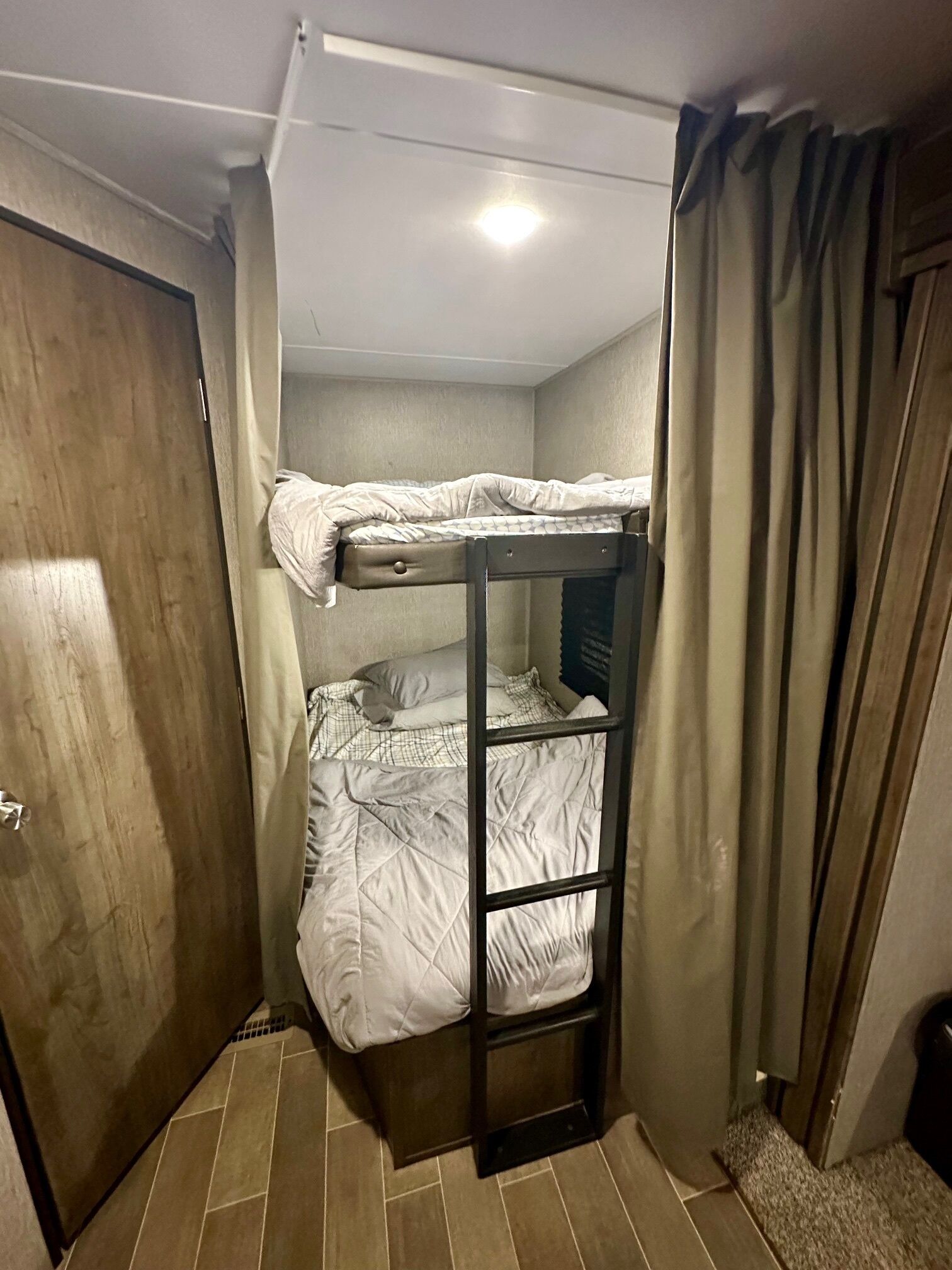 A bunk bed room with a door, a window with curtains, and a radiator.