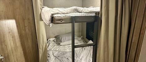 A bunk bed room with a door, a window with curtains, and a radiator.