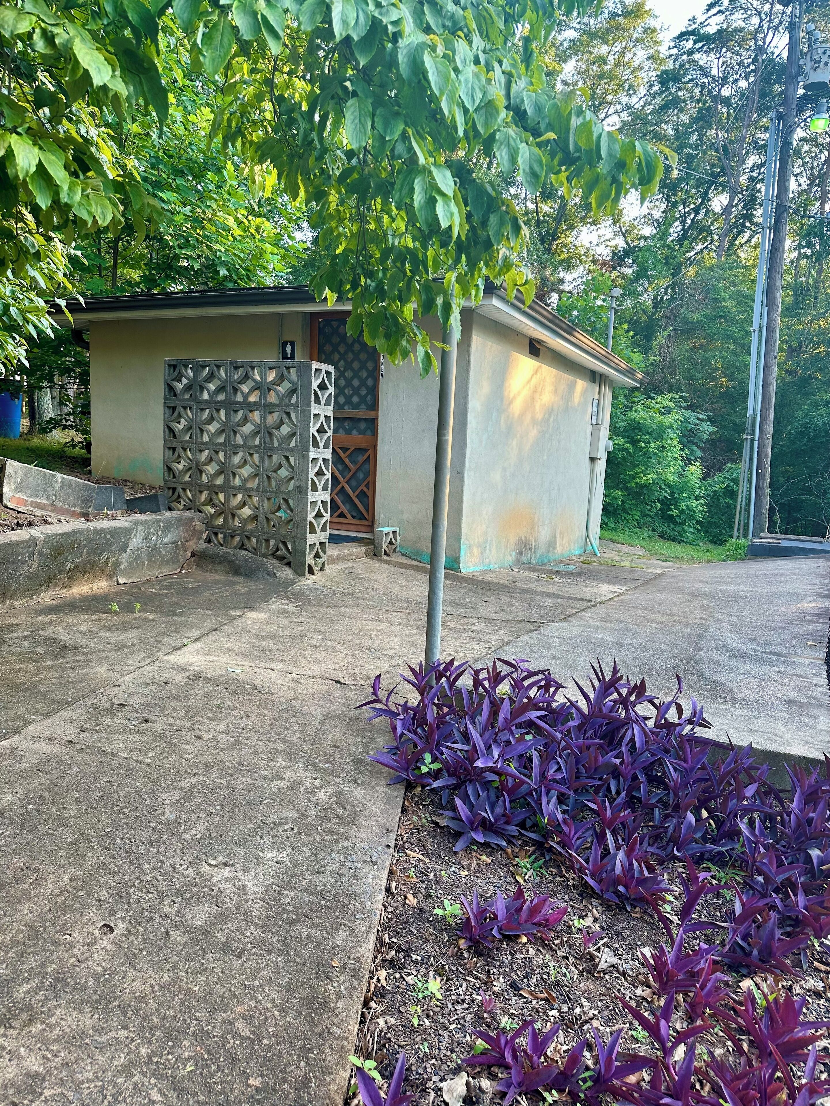A small building with a stone and metal gate, surrounded by a concrete area and purple plants.