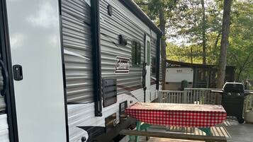 Een Coleman RV met een overdekte picknicktafel en een barbecue op een houten terras.