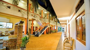 Un vestíbulo de hotel con una escalera central, varios balcones y suelo de arena.