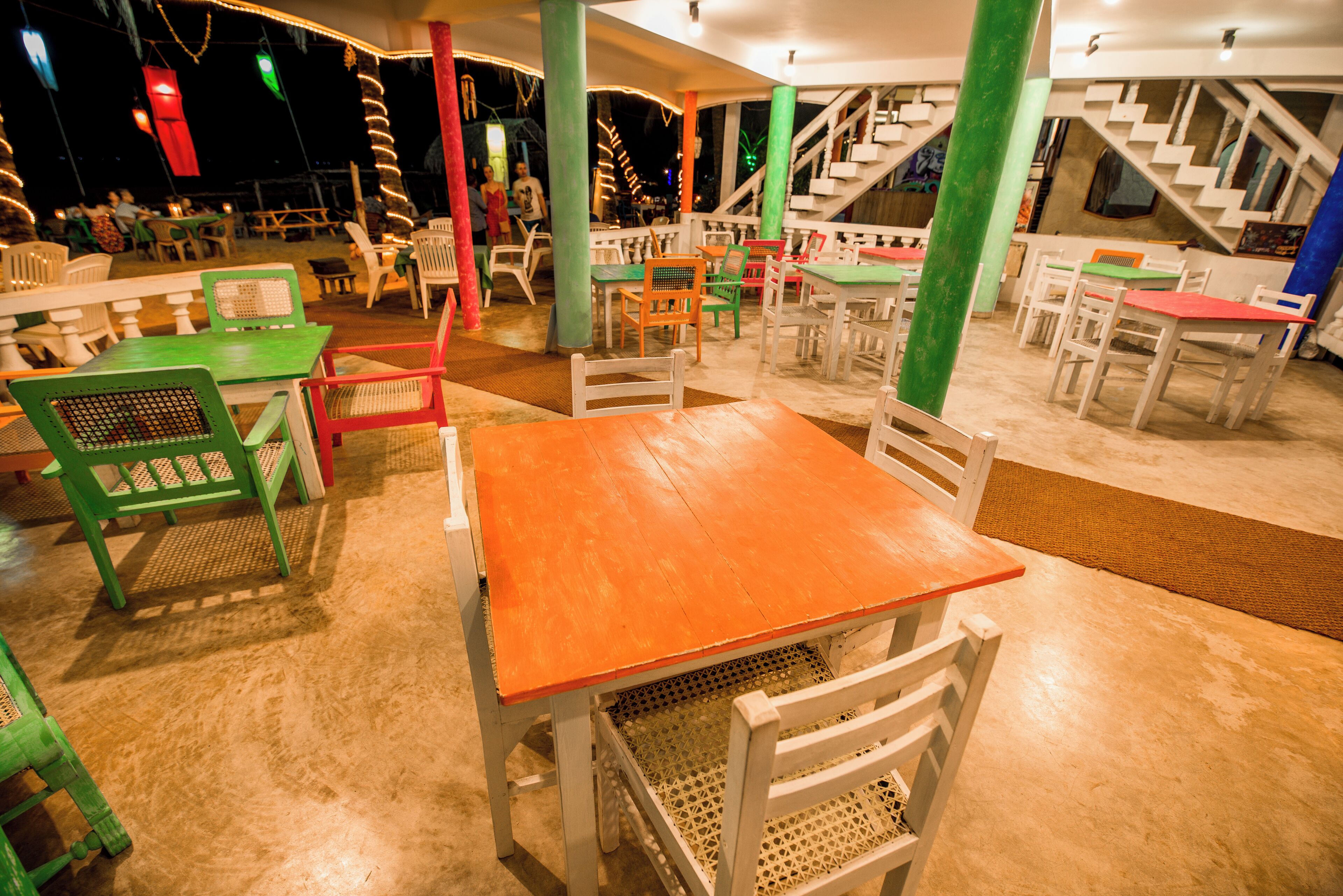 An indoor dining area with multiple tables and chairs, some with colorful upholstery.