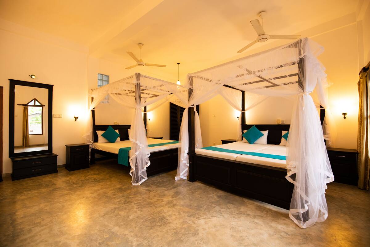A room with two beds, each with a canopy, a ceiling fan, and bedside lamps.