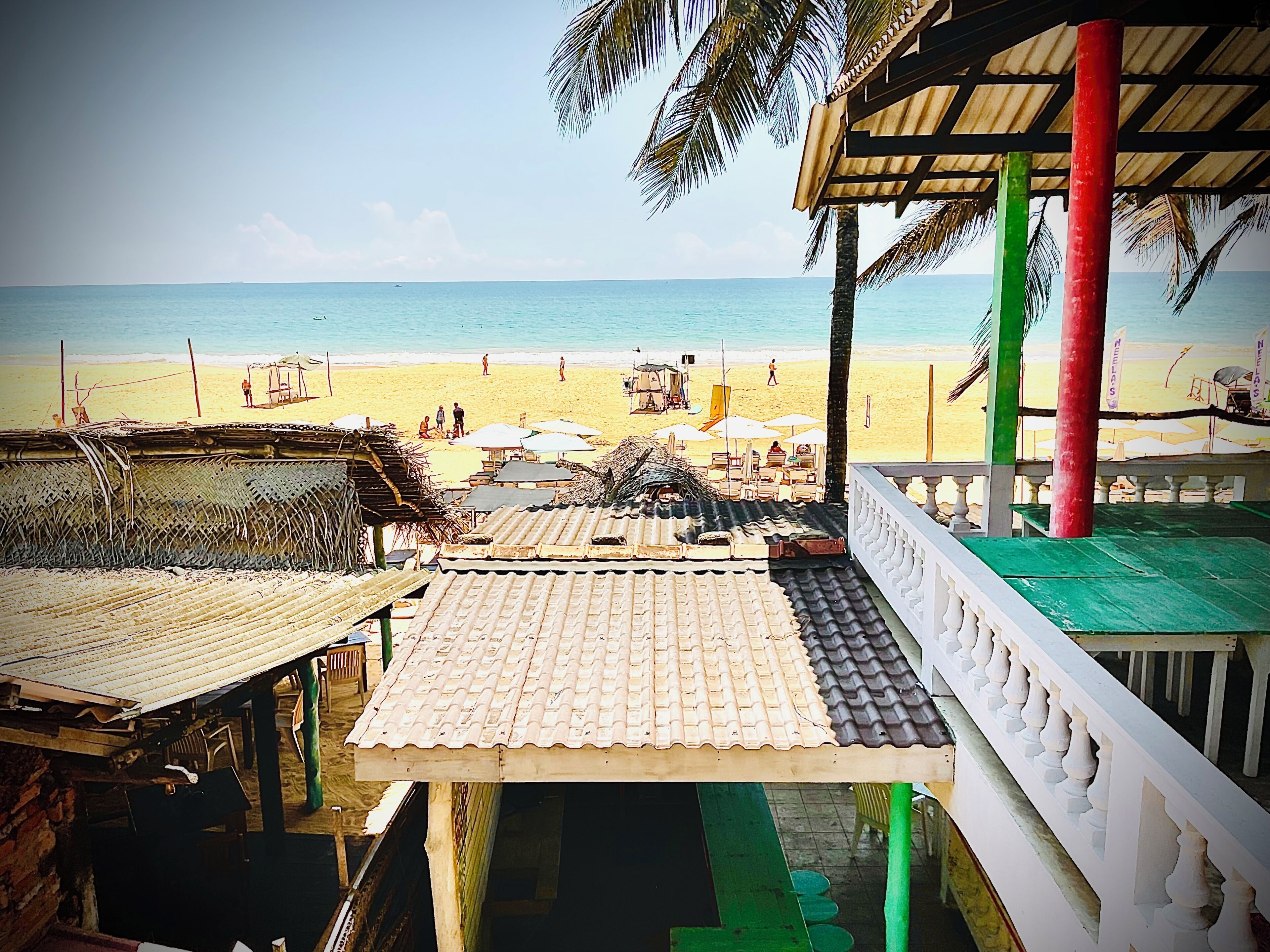 Une vue sur la plage depuis un espace abrité doté d’un toit de chaume, d’une terrasse en bois et offrant un panorama sur la plage et l’océan.