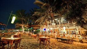 Un restaurante junto a la playa con terraza, palmeras y un letrero que dice 'DRU BAR'.