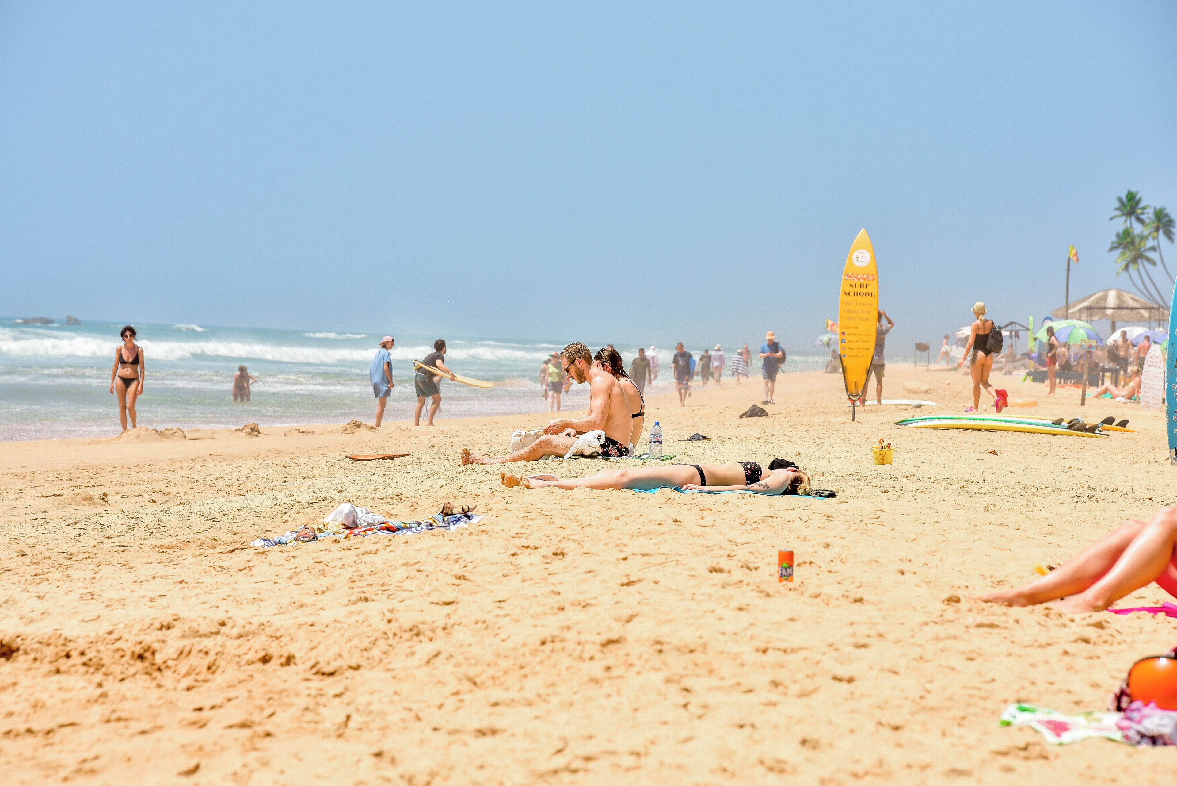 A beach scene with people sunbathing, swimming, and surfing.