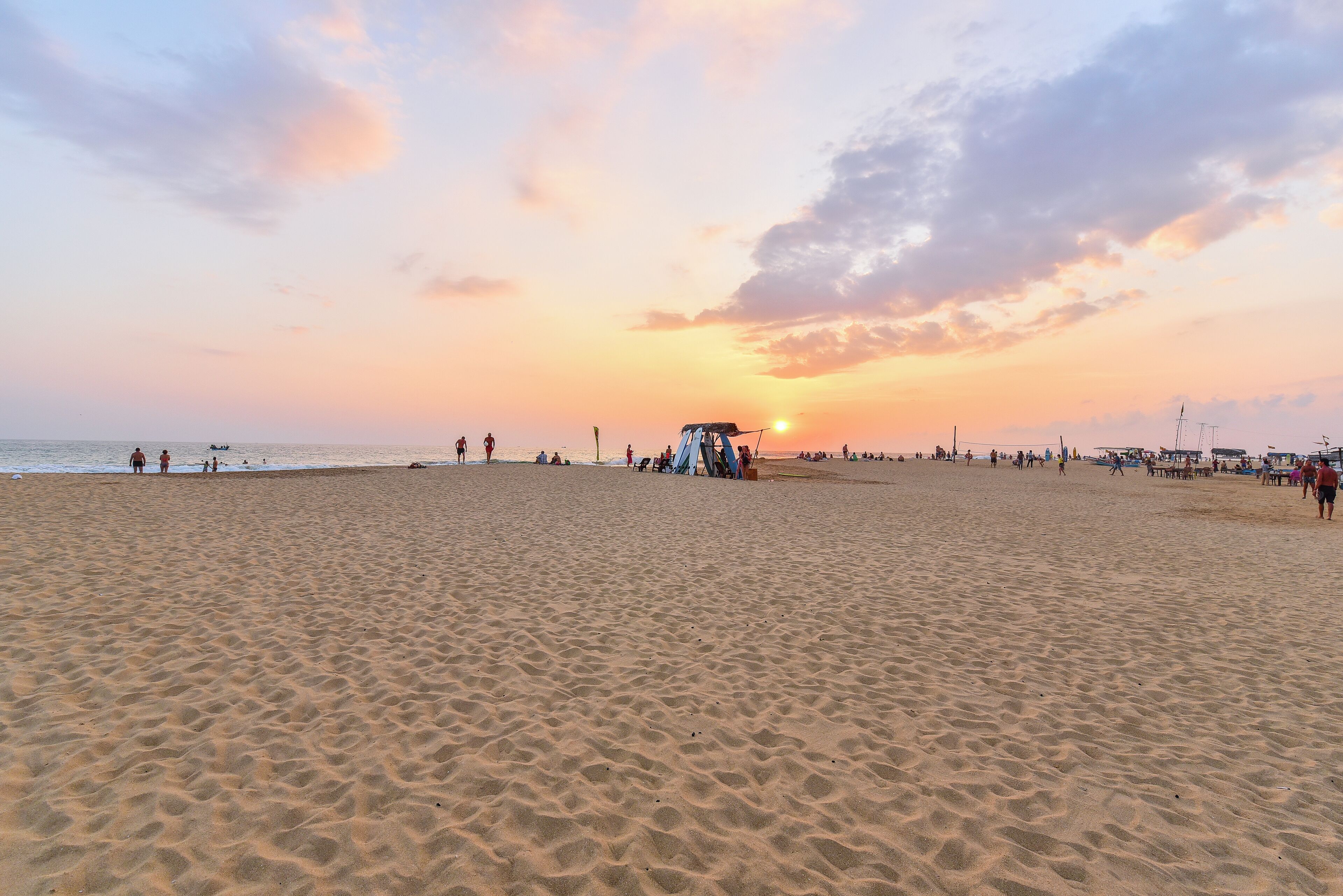 Una extensa playa arenosa con gente y una torre de salvavidas al atardecer.